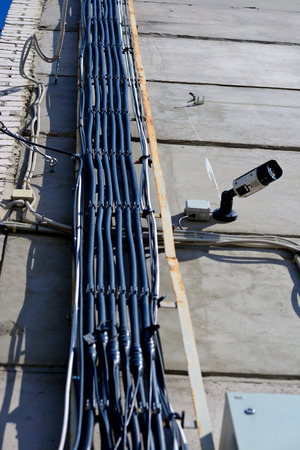 Cable tray run vertical up the wall looked from bottom view. Electric wires attached to a row on a concrete wall, near a surveillance cameraの写真素材