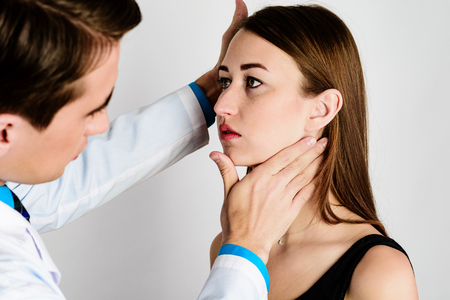 The doctor, a man, put his hand on the patient's neck to conditionally separate the lower jaw from the neck, to assess the severity of the profileの写真素材
