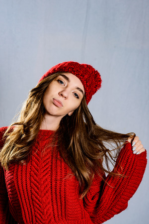 Fashionable young woman posing ,wearing red knitted sweater and red cap. Elegant woman wearing trendy outfit.Fashion portrait of beautiful young woman.の写真素材