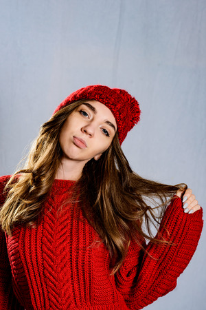 Fashionable young woman posing ,wearing red knitted sweater and red cap. Elegant woman wearing trendy outfit.Fashion portrait of beautiful young woman.の素材 [FY310123719384]