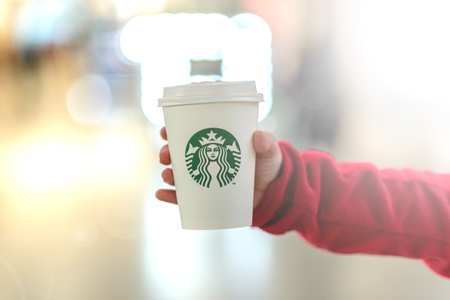 The child is holding a cup of Starbucks drink against the blurry lights of a shopping center. Russian Federation, Rostov-on-Don, April 12のeditorial素材