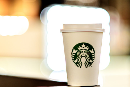 A white paper cup with coffee from Starbucks against the background of the blurry lights of the shopping center.  Russian Federation, Rostov-on-Don, April 13のeditorial素材