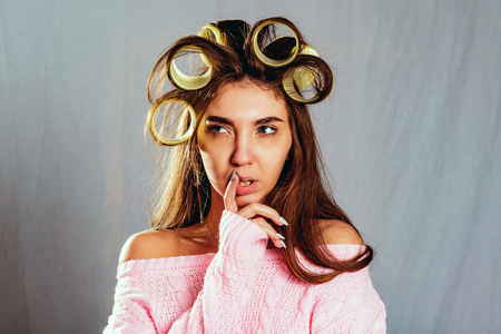 The portrait beautiful girl with curlers in her hair and a pink knitted sweater, isolated  on greyの写真素材