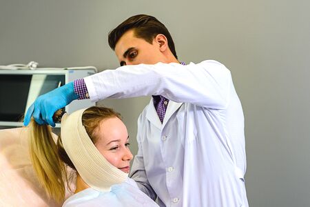 Doctor applying an elastic bandage on the contours of the face for gentle skin recovery after...