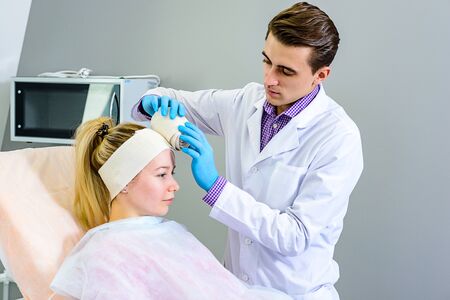 Doctor applying an elastic bandage on the contours of the face for gentle skin recovery after plastic surgeryの写真素材