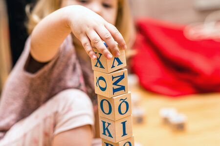 A baby is playing with wooden cubes with colored letters on the wooden floor of the background