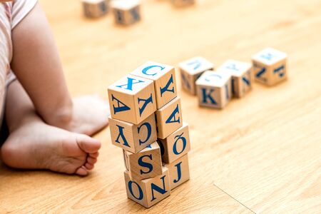 Ababy is playing with wooden cubes with colored letters on the wooden floor of the background