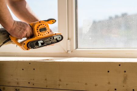 Carpenter's hands holding a belt sander against the window background