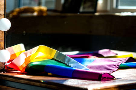 The multicolored flag of the LGBT community lies on the wooden countertop of the dressing table in front of the mirror, in the rays of the setting sunの写真素材