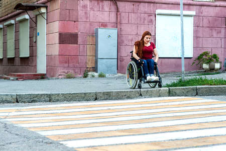 A young woman in a wheelchair passes through a pedestrian crossing at a green light.の写真素材