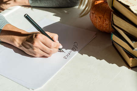 The woman's hand draws a close-up of English letters on a white sheet of paper. Calligraphic inscriptions by women's hands with a fountain pen under a bright light.の写真素材