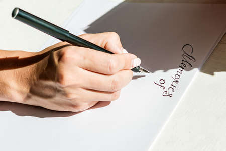 The woman's hand draws a close-up of English letters on a white sheet of paper. Calligraphic inscriptions by women's hands with a fountain pen under a bright light.の写真素材