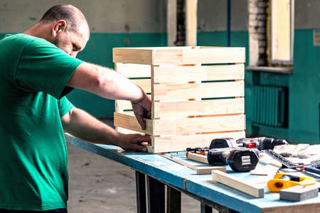 A young man in a green t-shirt works with wooden parts in a workshop.の写真素材