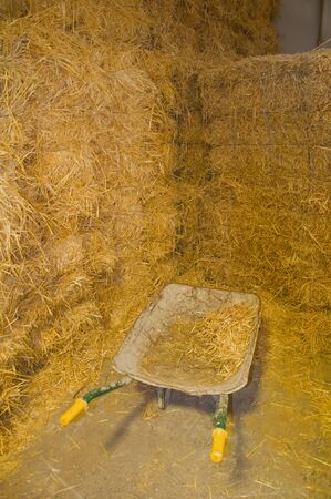 Metal wheelbarrow with yellow handles next to haystacks in the storehouse, Andalusia, Spainの写真素材