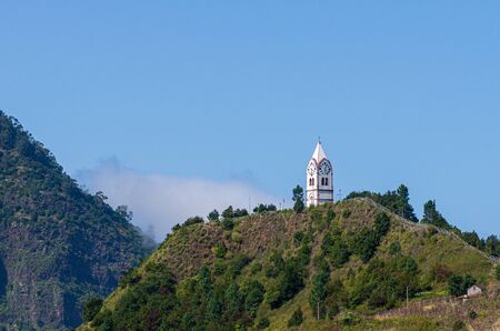 White church tower peeking behind a hill in Madeira Island