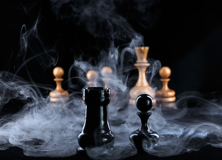 two black chess pieces in the fog opposite the white figuresの写真素材