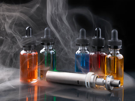 Electronic cigarette and vape liquids within vapor on black backgroundの写真素材