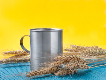 wheat spikelets and metal mug on bamboo mat. yellow backgroundの写真素材