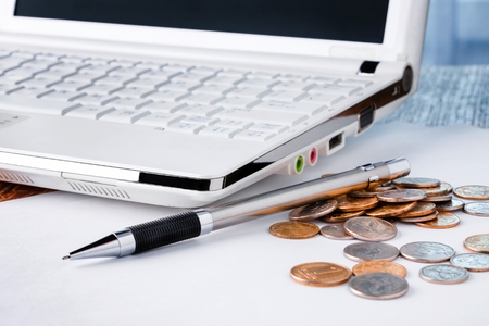 Close-up shot of laptop with pencil and heap of coins on wooden tableの写真素材