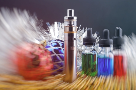 Electronic cigarette with vape liquids within vapor and christmas decorations on black background....