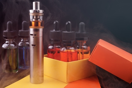 Electronic cigarette and vape liquids into opened gift box on fogged dark background. Toned lightの写真素材