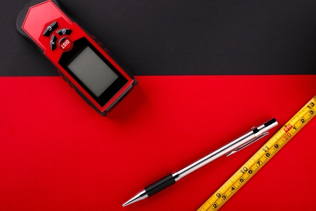 Tape measure, laser distance meter and pencil on matte black and red backgroundの写真素材
