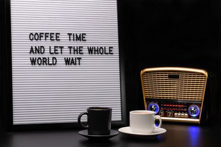 White and black cups of coffee, retro-styled radio receiver and letter board with inscription coffee time and let the whole world waitの写真素材