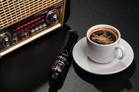 Radio receiver, cup of coffee and electronic cigarette on black surfaceの写真素材