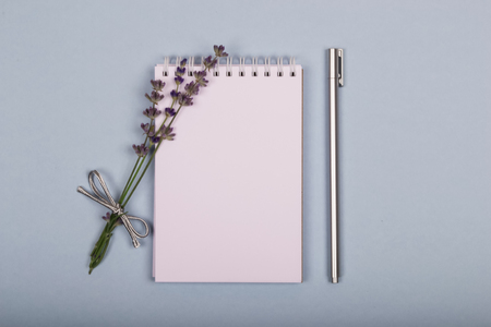 White notepad on a blue background with a small bouquet of purple lavender and a silver pen lying on it.の写真素材