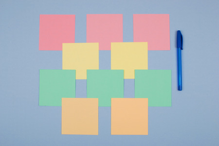 Note paper laid out in a symmetrical blue, pink, green, orange on a blue background. Nearby is a blue pen.の写真素材