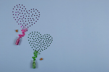 Spangles spilled from small glass bottles in the form of two hearts of green and pink color on a blue background.の写真素材
