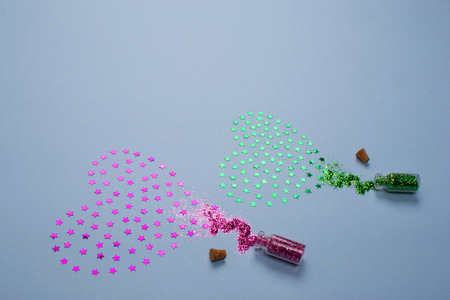 Spangles spilled from small glass bottles in the form of two hearts of green and pink color on a blue background.の写真素材