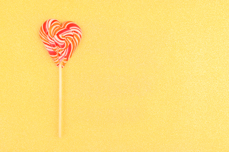 A striped heart-shaped lollipop on a gold background.の写真素材