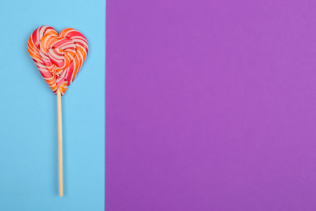 A striped heart-shaped lollipop on a blue background.の写真素材