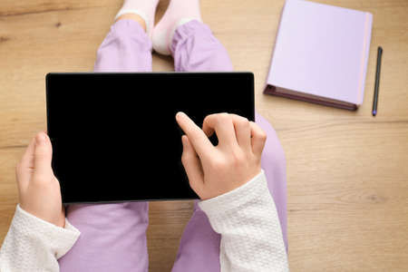 Child with a tablet, tap with a finger, touchscreen on a light wooden background. Modern technologies. Education concept. Tablet, distance learning. Homework, self-education. Child development, study. The concept of the development of mental abilities.の写真素材