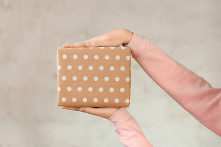 Box in hands on a light background. Beige gift. White peas. Female hands with place for text. Surprise, holiday concept. Mother's Day, International Women's Day, Birthday. Gift selection, online shopping, sale.の写真素材