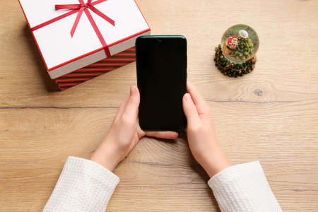 Hands hold a phone on a wooden background, Ordering gifts via the Internet. Internet - shopping, sale, black friday. Christmas spirit, holiday concept, surprises for children. Gifts for the New Year. The gadget is in children's hands.の写真素材