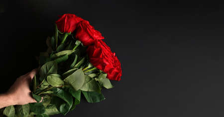 Man with a big bouquet of flowers on a black background. Surprise from a beloved. Gift of St....