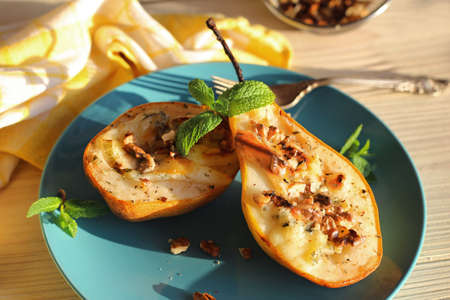 Ready-made dessert of baked pears, dor blue cheese, nuts and honey. Vegetarian pear dessert in a plate on a wooden surfaceの写真素材