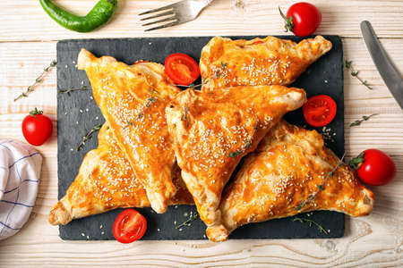 triangular puffs with feta cheese, tomatoes, herbs on a structural wooden background with place for...