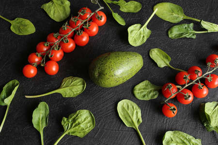 Fresh spinach leaves, cherry tomatoes and ripe avocado on a dark stone background top view. Ingredients for the salad. Healthy food, diet food.の写真素材