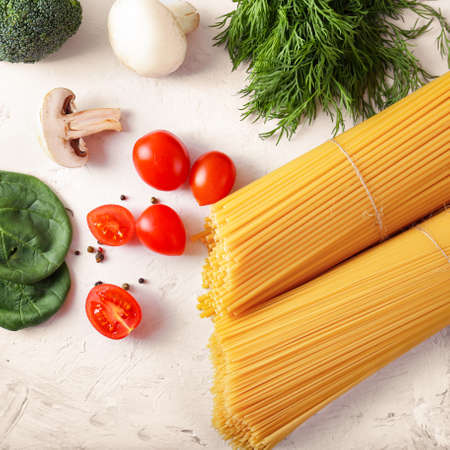 Top view of raw spaghetti on light background. Italian food ingredients. Pasta, tomatoes and spices.の写真素材