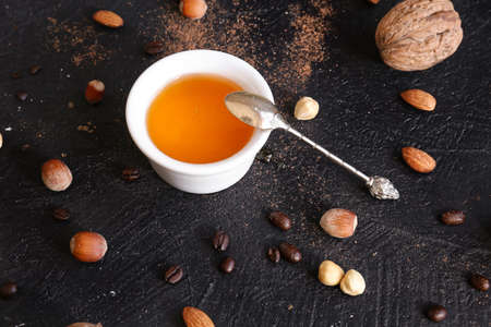 Honey in a plate and nuts scattered around on a dark background. Hazelnuts and Almonds. Honey in a glass bowl with a spoonの写真素材