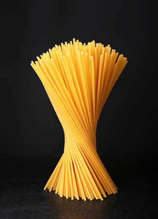 Raw spaghetti on dark background. Uncooked pasta with copy space. A bunch of spaghetti stands on a black surfaceの写真素材