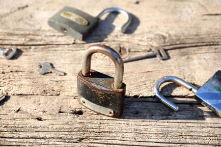 Vintage rusty padlocks surrounded by different keys on a weathered wooden background. Concept of many wrong options. The concept of lack of right option.の写真素材
