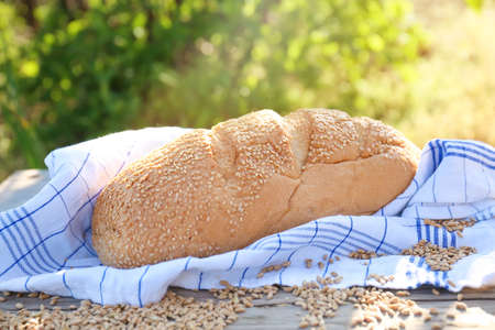 Loaf of freshly baked bread on a tablecloth on a wooden table. Scattered grains of wheat. Bread as a...
