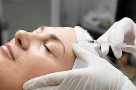 Young caucasian woman getting botox cosmetic injection in a forehead. Beautiful woman gets botox injection in her face. Adult girl gets cosmetic injection of botox in a clinic. beauty treatmentsの写真素材