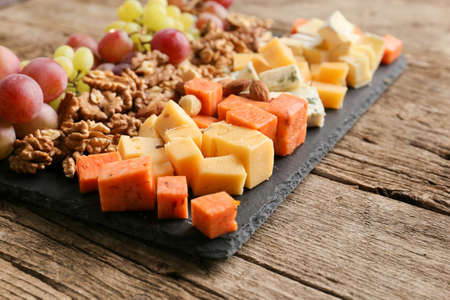 Different types of delicious cheese, nuts, grapes on a wooden background. Cheese platter: brie, camembert, blue cheese, emmental, parmesan, goat cheese, honey, grapes, walnuts, almonds. Healthy food. Fresh appetizing snack.の写真素材