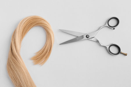 Scissors and piece of blond hair. Professional barber hair cutting shears on background. Hairdresser salon equipment concept, premium hairdressing set. Accessories for haircut with copy spaceの写真素材