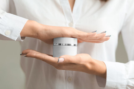 Hands of young woman holds hand skincare cream. Woman model with body cream jar in hands. Winter skin care and wellness concept. Close-up closed jars of cream in hands. The beautician holds products in the form of jars of cream.の写真素材